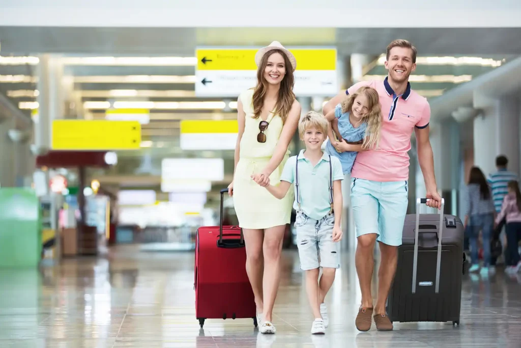 A smiling family with suitcases walking relaxed through a bright airport departure hall.