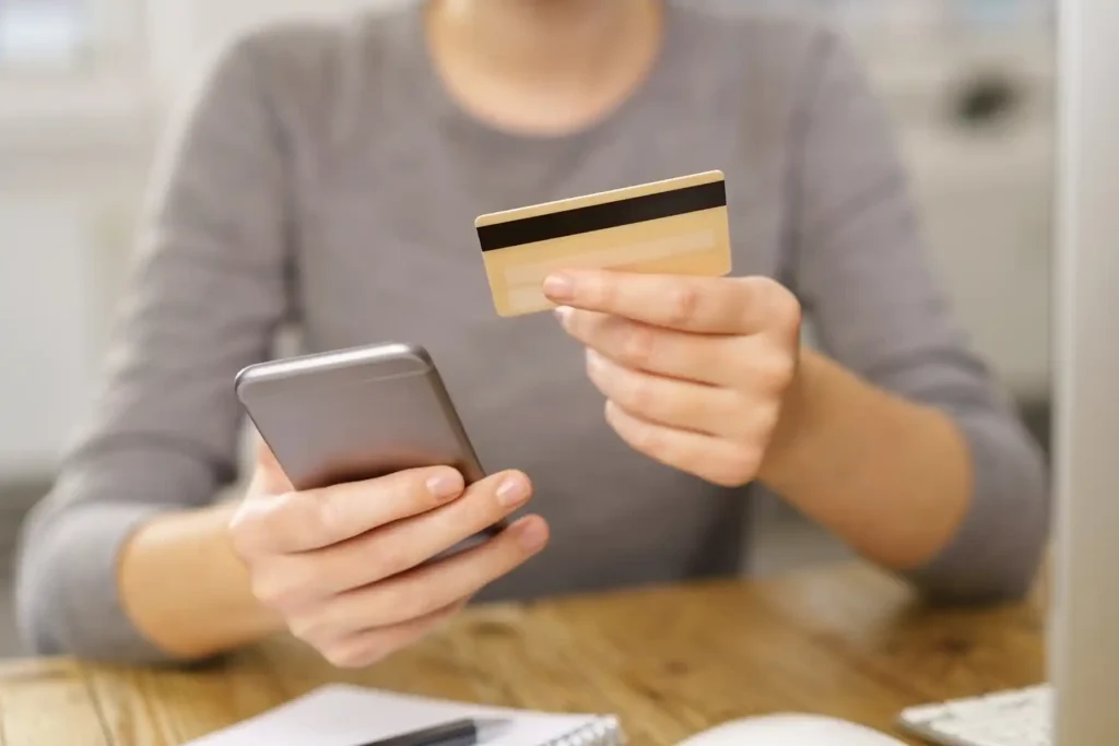 Close-up of hands making an online reservation using a smartphone and a credit card.